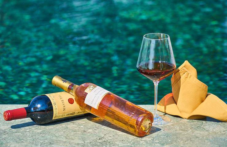 Due bottiglie di vino e un calice appoggiate su un muretto in riva al mare