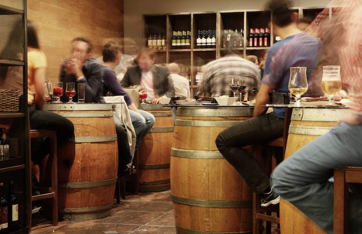 Persone sedute intorno a delle botti di vino usate come tavoli per delle degustazioni