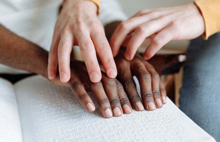 Quattro mani che leggono un libro di Braille