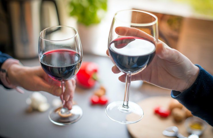 Due persone che brindano con due calici di vino rosso