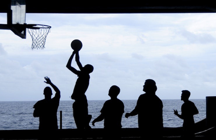 Persone giocano a basket, con il mare sullo sfondo