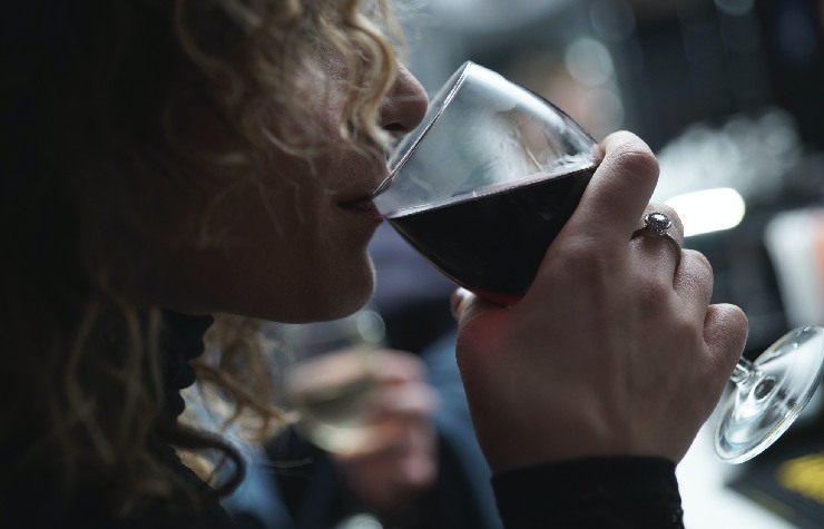 Donna ricciola che beve da un calice di vino rosso